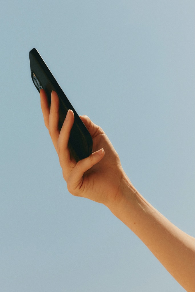 A hand holding a phone against a blue sky